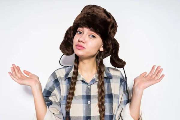 Funny young Russian girl in a warm cap with ear-flaps waving her hands — Stock Photo, Image