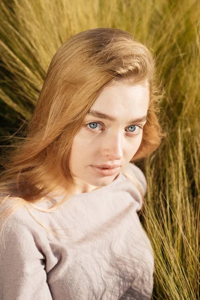 Jovem de olhos azuis menina loira modelo posando, sentado em um campo ao sol — Fotografia de Stock
