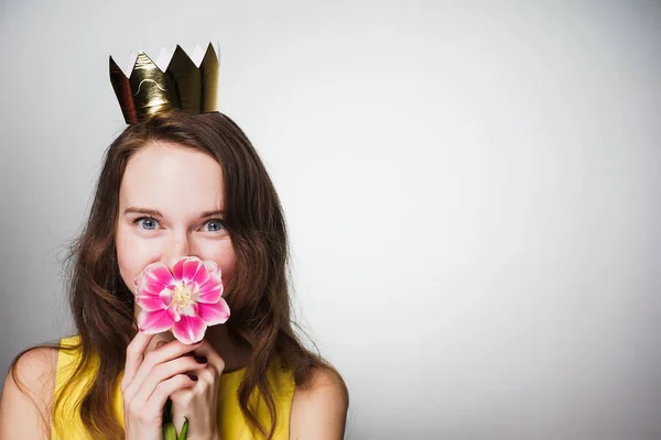 Feliz joven con una corona dorada en la cabeza oliendo una flor rosa celebrando el día mundial de la mujer — Foto de Stock