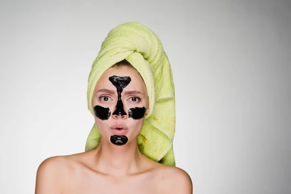 Una giovane ragazza indignata con un asciugamano verde sulla testa ha applicato una maschera nera alle zone problematiche sul suo viso — Foto Stock