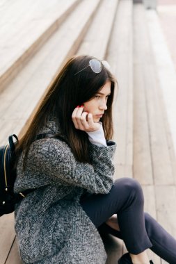 şık güzel esmer şehir kızı gri paltolu belgili tanımlık merdiven üstünde oturur ve bir yere benziyor