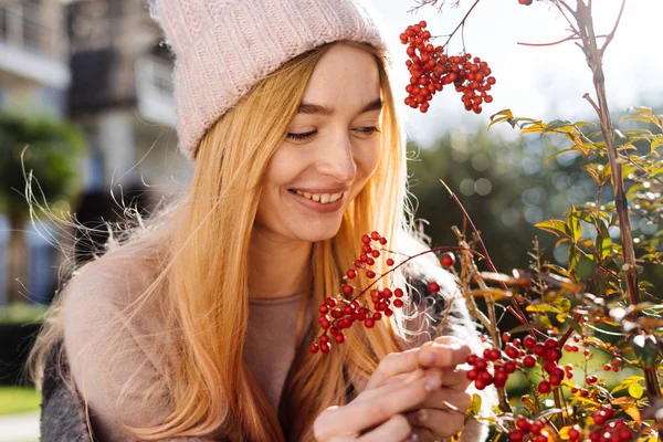 Glad ung tjej blond i en rosa hatt som tittar en berry, leende, promenader genom trädgården — Stockfoto