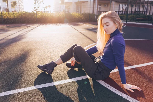 Стильна красива блондинка модель дівчина в синьому светрі сидить на спортивному полі на сонці — стокове фото