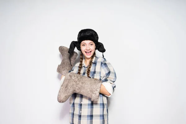 Lustiges Smiley russisches Mädchen mit schwarzem Hut und Ohrenklappen hält graue Winterstiefel — Stockfoto