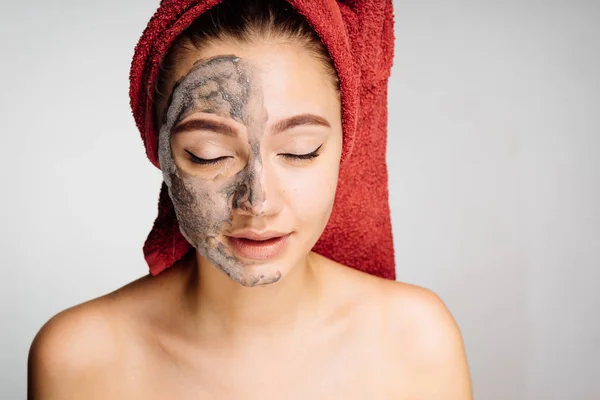 A cute young girl enjoys spa treatments, put a clay mask on half of her face, her eyes are closed — Stock Photo, Image