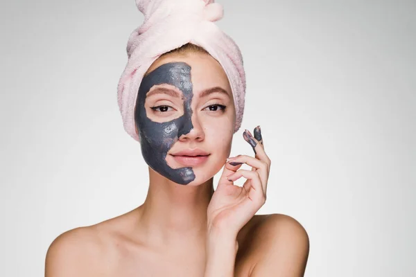 Μια ελκυστική κοπέλα με μια ροζ πετσέτα στο κεφάλι της εφαρμόζεται μια χρήσιμη άργιλος μάσκα μισού προσώπου — Φωτογραφία Αρχείου
