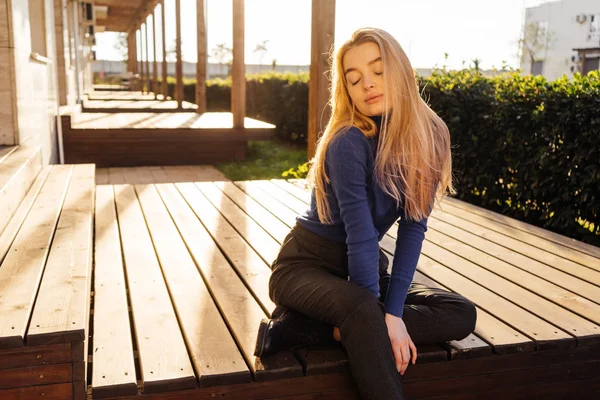 Atraente jovem loira modelo menina em elegante camisola azul posando ao sol ao ar livre — Fotografia de Stock