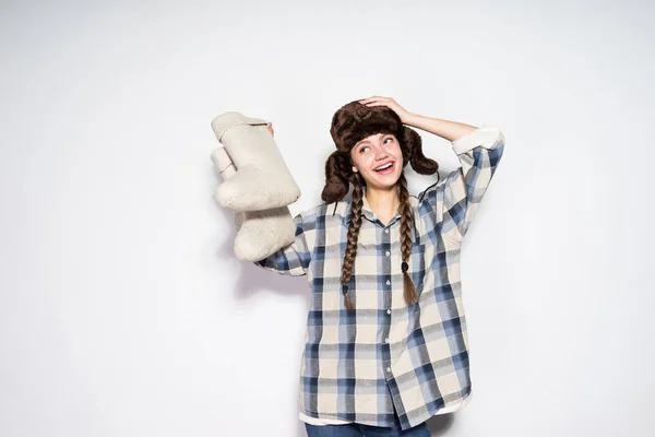 Glücklich lächelnde russische Mädchen in einem warmen Hut mit Ohrenklappen hält graue Filzstiefel — Stockfoto