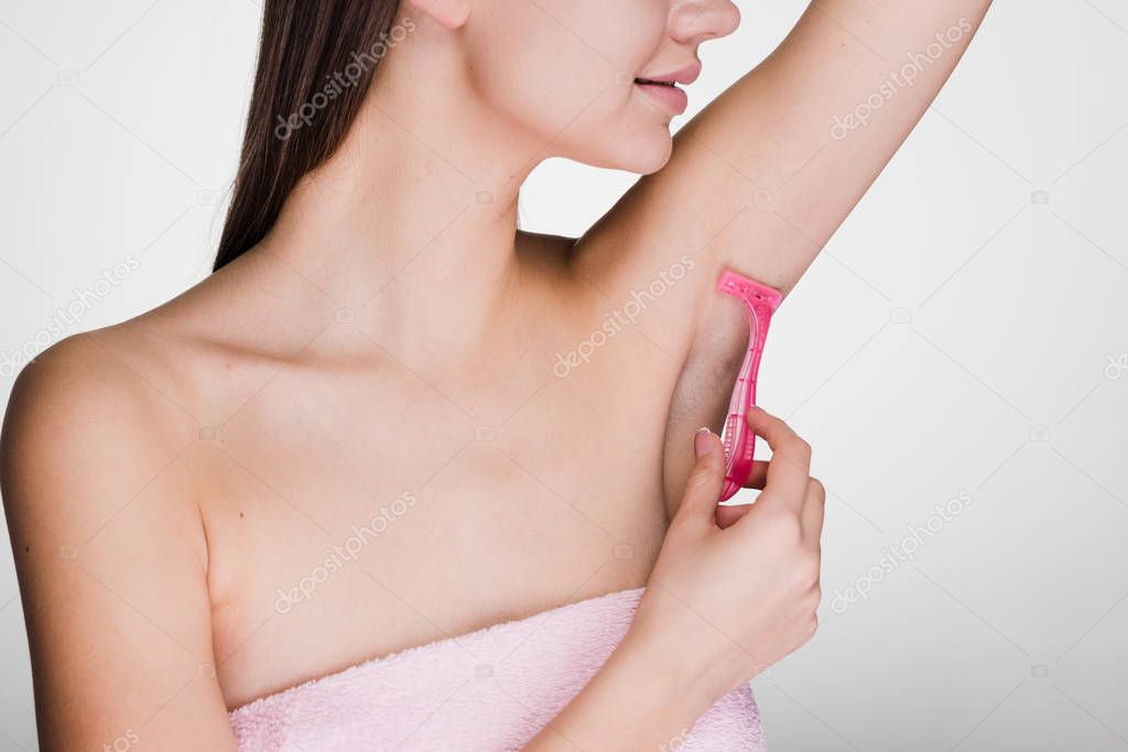 cute young girl shaves her hair on her armpits with a pink razor