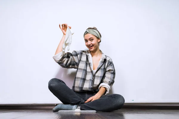 Gelukkig jong meisje in een shirt zit op de vloer, doen van reparaties in haar appartement, bedrijf van een rubberen handschoen — Stockfoto