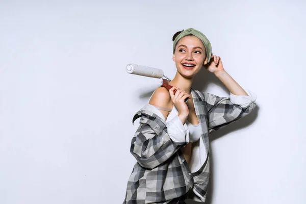 Een mooie jonge vrouw in een shirt schildert de muren met een roller in haar nieuwe appartement — Stockfoto