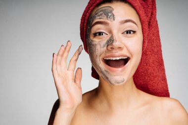 başında kırmızı bir havlu ile mutlu genç kız bir kil maskesi onun yüz, gülüyor, spa prosedürler yarısı için uygulanan