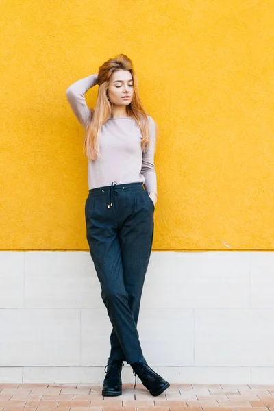 Mooie jonge blonde meisje in stijlvolle blauwe jeans poseren tegen een gele muur achtergrond — Stockfoto