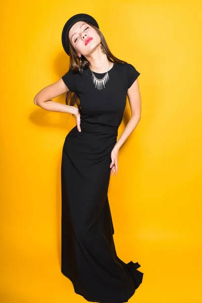 검은 드레스와 모자 노란색 배경에 포즈에 고급 스러운 매력적인 여자 — 스톡 사진