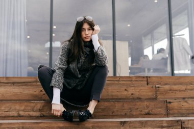 poz merdivenlerde, şık genç kız siyah saçlı ve gri paltolu oturur