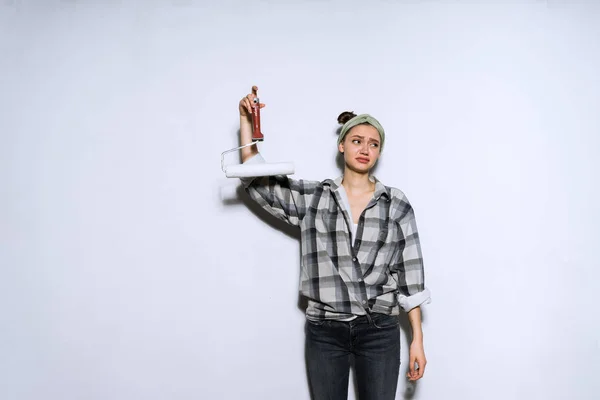 Insoddisfatto giovane ragazza in camicia stanco di fare le riparazioni, tiene rullo per la pittura pareti — Foto Stock