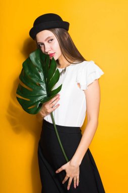 çekici genç kız modeli şık siyah şapkalı yaprak yeşil holding, sarı arka plan üzerinde poz