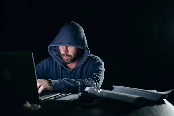 Misterioso criminoso homem em um capuz invade um laptop no escuro — Fotografia de Stock