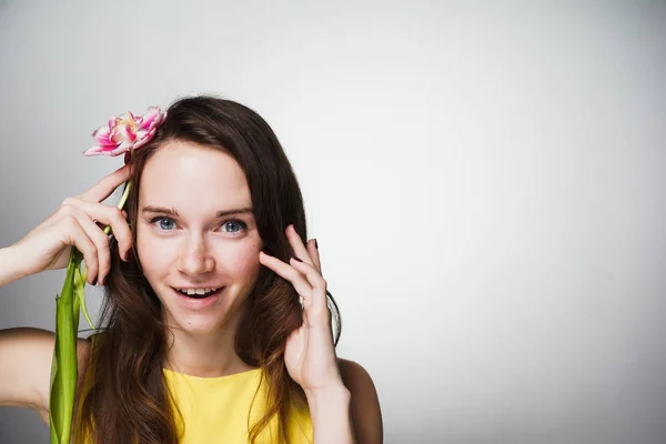 Hermosa joven en vestido amarillo sostiene flor fragante, celebra el día de la madre y sonríe — Foto de Stock