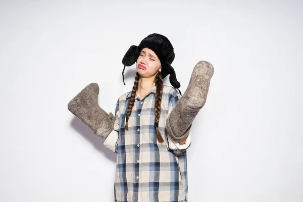 Triste giovane ragazza russa in un cappello nero con paraorecchie tiene stivali di feltro caldo inverno — Foto Stock