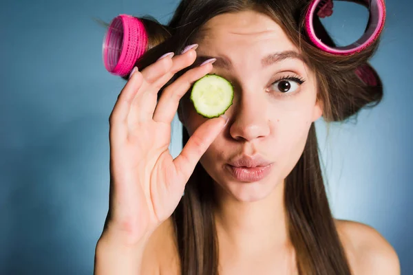 Söt ung tjej vill se bra ut, på huvudet av locktången, håller gurka för att återfukta huden i ansiktet — Stockfoto