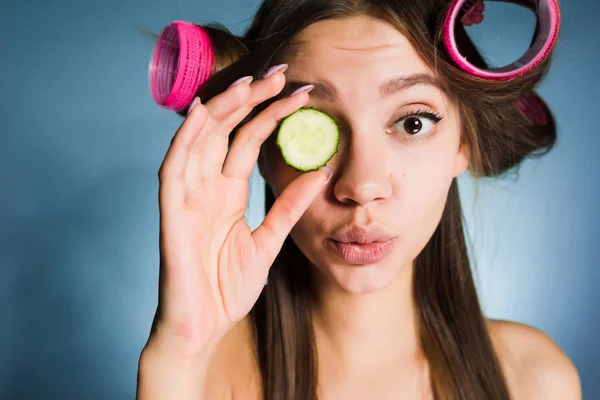 Bonito jovem quer olhar bom, na cabeça do curler, mantém o pepino para hidratar a pele do rosto — Fotografia de Stock