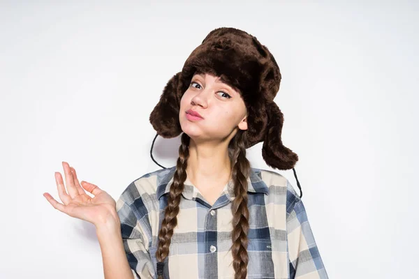 En morsom, ung russisk jente i en varm hatt med øreklaffer som spyttet seg i kinnene – stockfoto