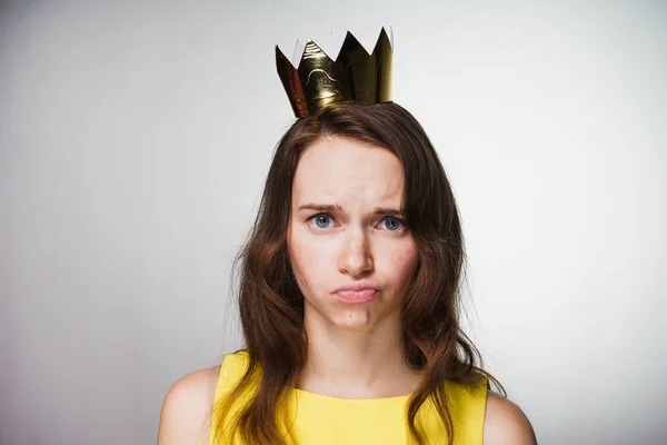 Mujer joven descontenta con un vestido amarillo mira a la cámara, sobre su cabeza una corona dorada — Foto de Stock