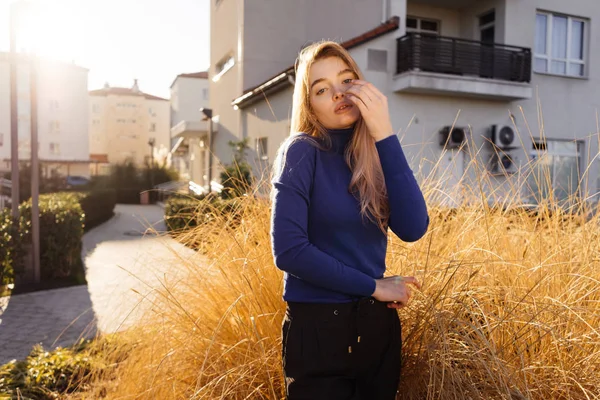 Elegante ragazza bionda in maglione blu passeggia per la città, in posa al sole — Foto Stock