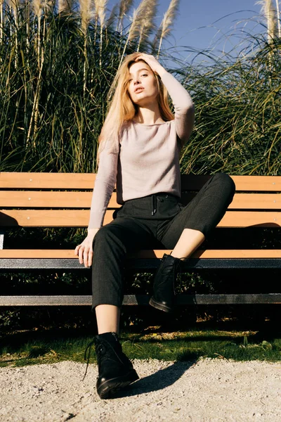 Stijlvolle jong blond meisje zit op een bankje buiten, poseren in de zon — Stockfoto