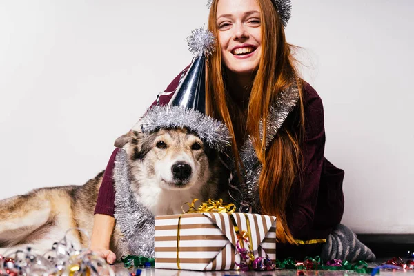 Happy young red-haired girl sits on the floor with her dog, celebrates the new year and christmas — Stock Photo, Image