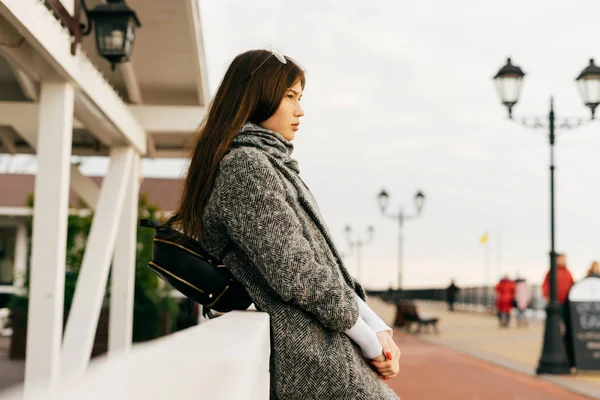 Stylish dark-haired girl in gray coat walking through city streets posing — Stock Photo, Image