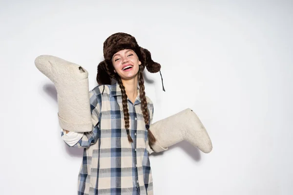Glücklich lächelnde russische Mädchen in einem warmen Hut mit Ohrenklappen hält Winterstiefel — Stockfoto