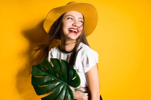 Roześmiany szczęśliwy dziewczyna model w modny kapelusz posiada zielony liść, na żółtym tle — Zdjęcie stockowe
