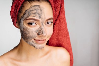 Kafasındaki bir havlu ile güzel bir genç kız bir yararlı kil maskesi yarım yüze uygulanan Spa gün