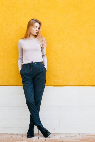 Stylish cute blonde girl walking, posing against a yellow wall background — Stock Photo, Image