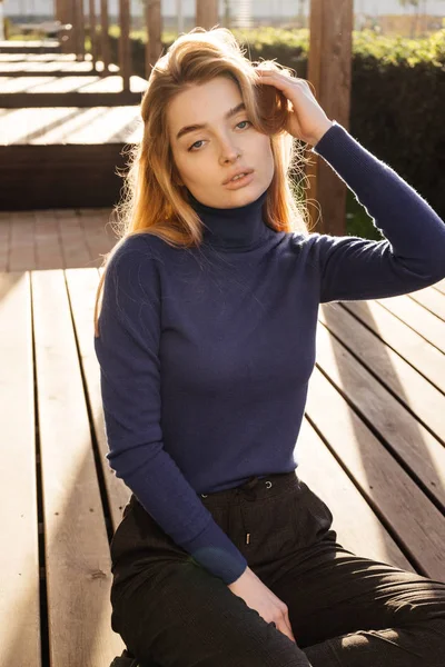 Mooie jonge blonde meisje in blauwe stijlvolle trui poseren buiten in de zon — Stockfoto