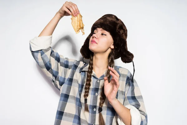 Een mooi Russisch meisje in een bont muts met een bont hoed een carnaval viert, eet een warme heerlijke pannenkoek — Stockfoto