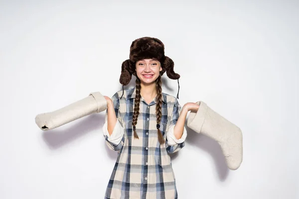 Улыбающаяся молодая девушка из России в теплой меховой шляпе держит серые войлочные сапоги в руках — стоковое фото
