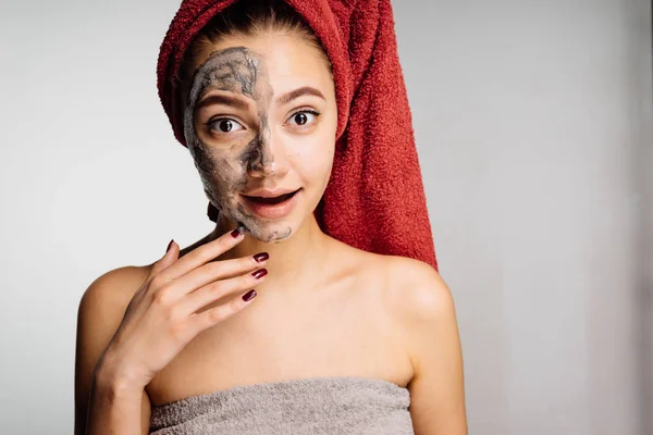 A woolly surprised girl with a towel on her head applied a useful mask to half the face, spa procedures — Stock Photo, Image