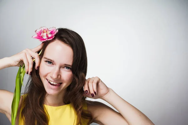 Glad skrattande ung kvinna i gul klänning innehar rosa blomma, firar Mors dag — Stockfoto