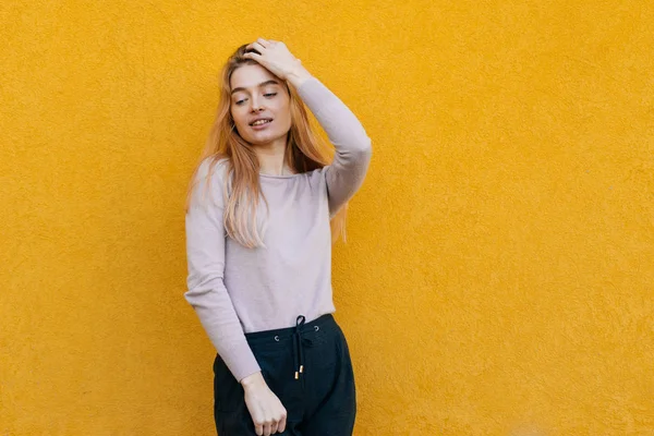 Hermosa joven rubia sonriendo, posando sobre el fondo de la pared naranja — Foto de Stock