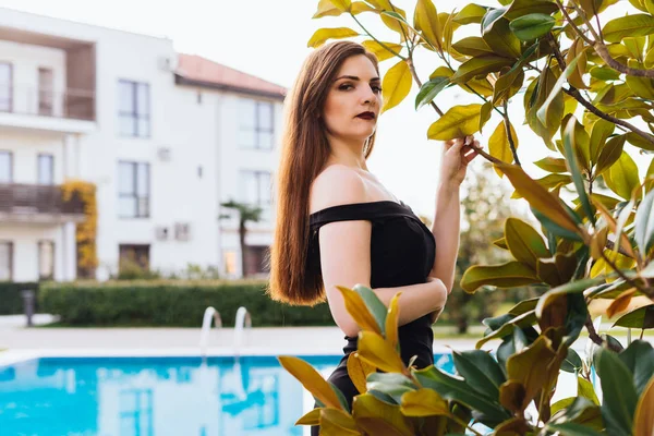 Sexy lussuosa giovane donna in un abito nero in posa, godendo di un ricco vertigini e relax, in piscina — Foto Stock