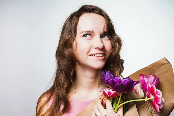 Vacker ung kvinna som håller en bukett blommor, leende och tänka på semestern, en internationella kvinnodagen — Stockfoto