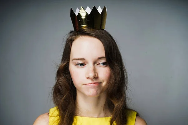Una joven pensativa en un vestido amarillo está esperando el Día de la Madre, en su cabeza hay una corona de oro — Foto de Stock
