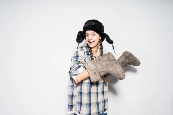 Una joven de Rusia riéndose con un sombrero caliente sostiene botas de invierno en sus manos — Foto de Stock