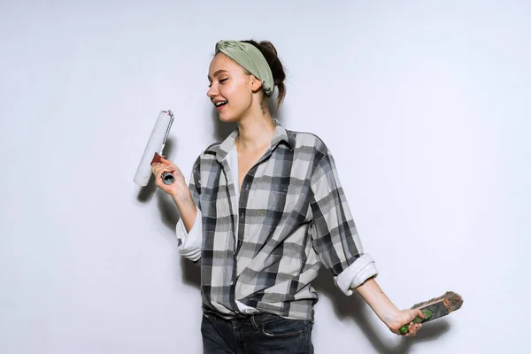 Счастливая молодая девушка рисует стены в белом, делает ремонт в квартире, держит кисть и веревку — стоковое фото