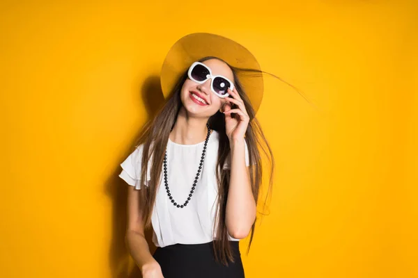 Sorrindo menina elegante em chapéu de moda e óculos de sol posando no fundo amarelo — Fotografia de Stock