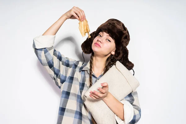 La ragazza affamata dalla Russia in un cappello di pelliccia mangia frittelle deliziose calde, celebra Shrovetide — Foto Stock