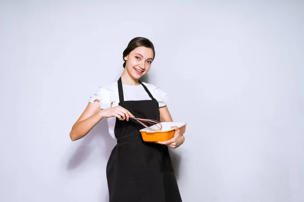 Красива молода жінка готує в чорному фартусі готує смачну їжу, посміхаючись — стокове фото